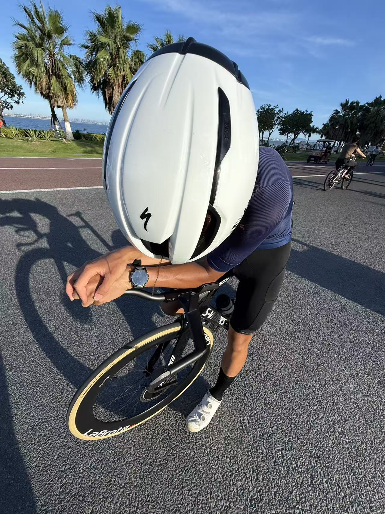 Louis in an aero helmet resting on a black TT bike by the seaside
