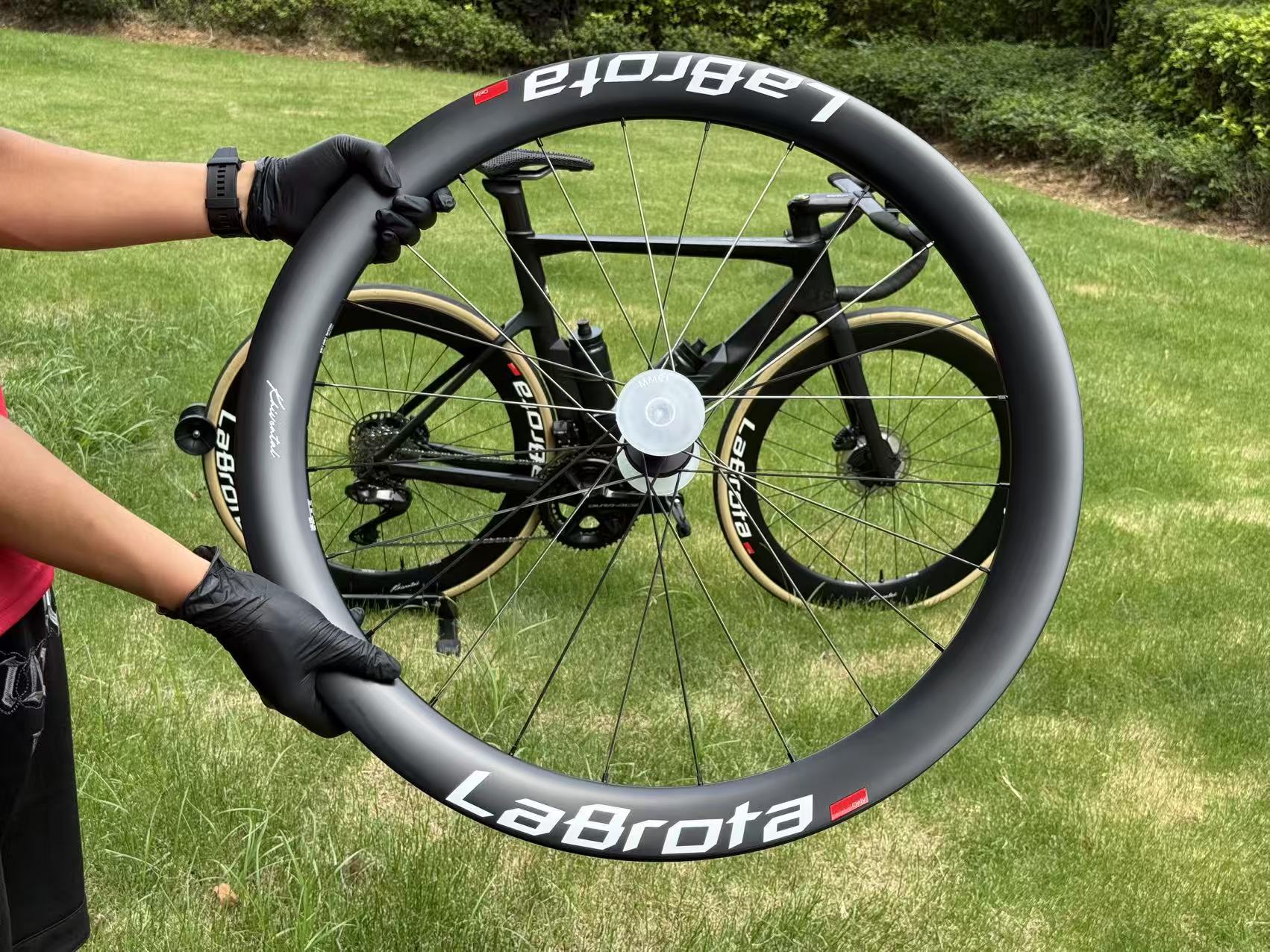 A LaBrota front wheel held up by hand in front of Louis’s black bike on grass