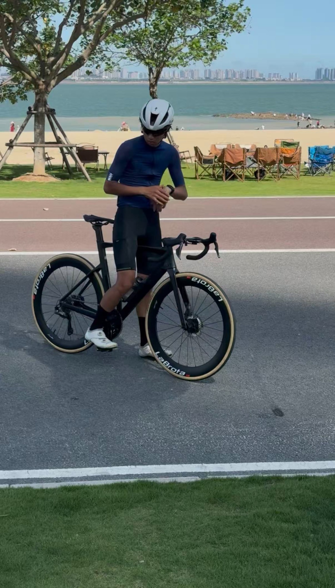 Louis standing beside a matte-black BMC road bike with LaBrota wheels near the beach