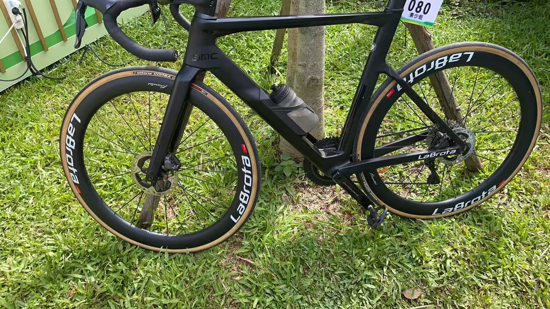 A matte-black BMC road bike with LaBrota wheels leaning on grass