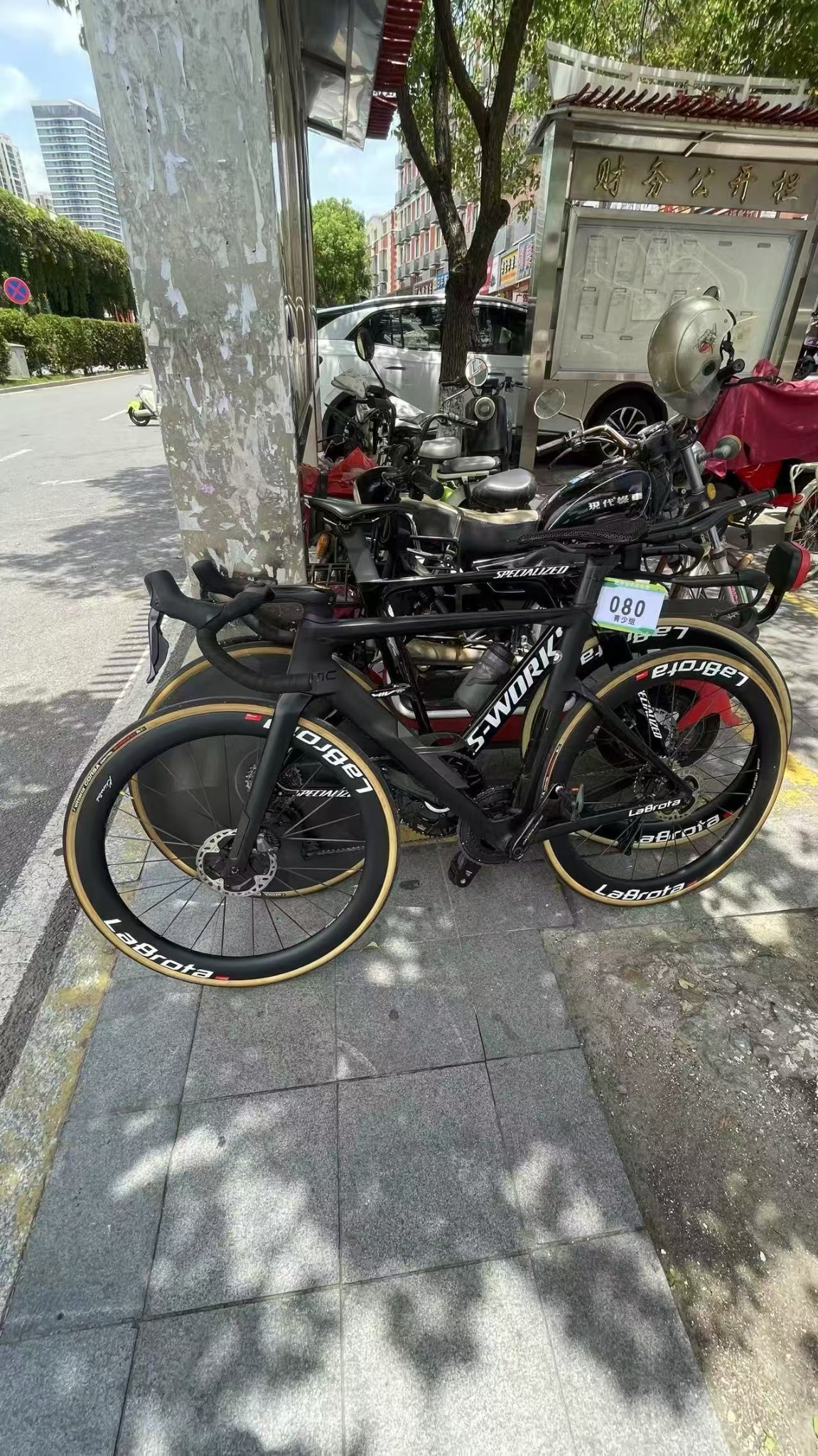 A black S-Works bike with LaBrota front wheel parked roadside with race plate 080